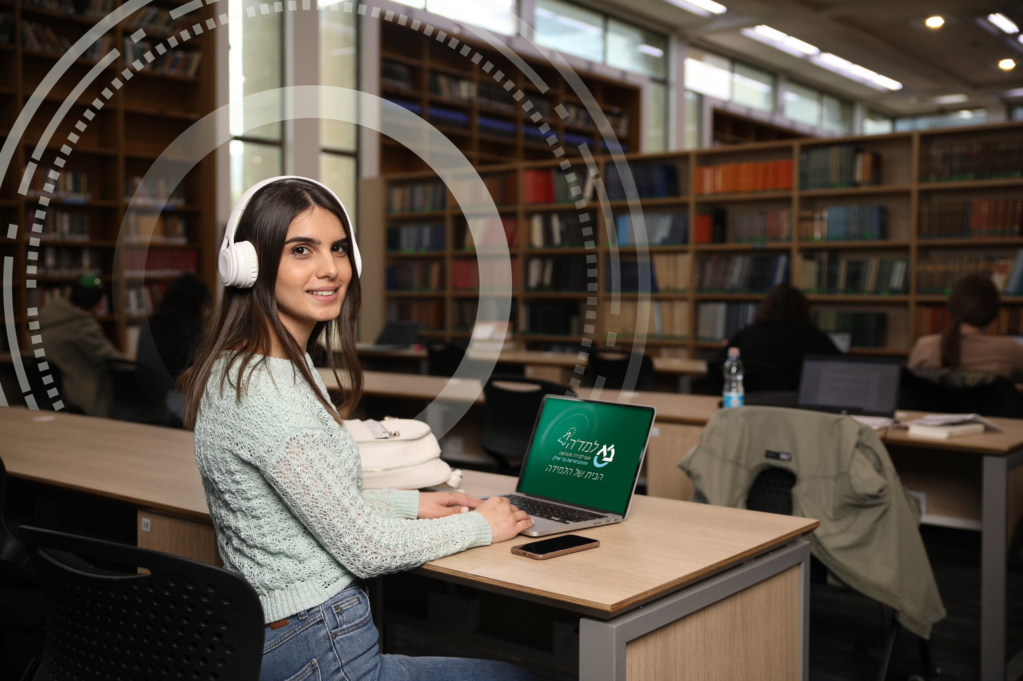 a female student sitting in a library wearing headphones. a laptop in front of her
